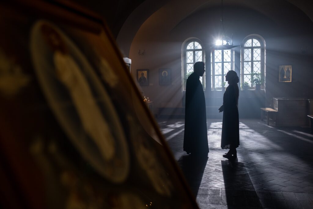 A priest and parishioner silhouetted during a conversation in a sunlit church interior.