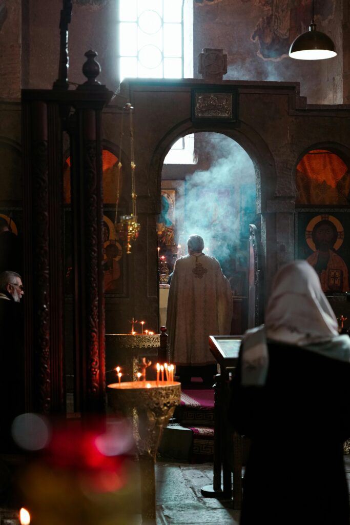 A priest conducts a religious ceremony in a Tbilisi church with candles and smoke.